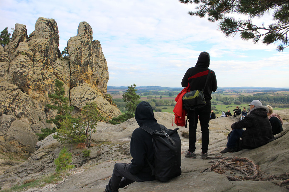 Mehrere junge Menschen auf einem steinigen Hügel sitzend, blicken in den Horizont.
